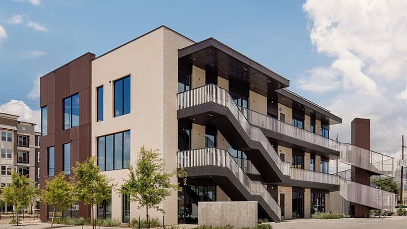 Exterior view of 3509 Harrisburg, showcasing a modern architectural design with warm metal finish, Mature Rust and a sleek blackened steel finish, Gun Metal, set against an urban backdrop.