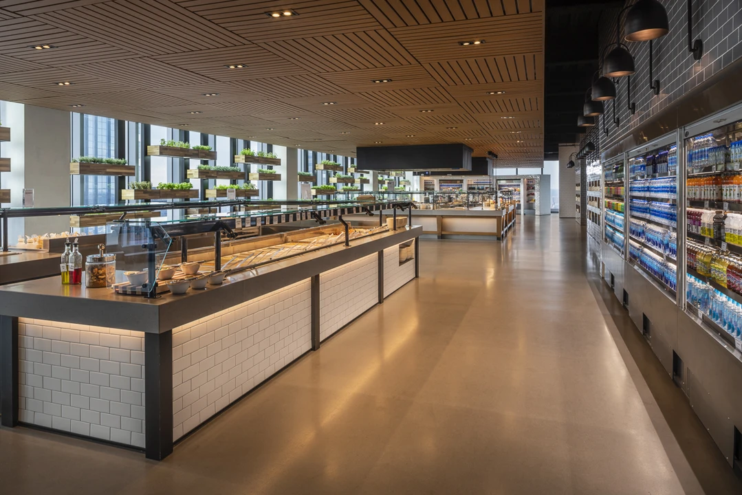 ComcastCenterMarket_InterierCeiling_LinearClipStrip_Woodgrain4 Modern cafeteria interior featuring a Channel™ ceiling system with linear aluminum ceiling panels in a warm wood finish.
